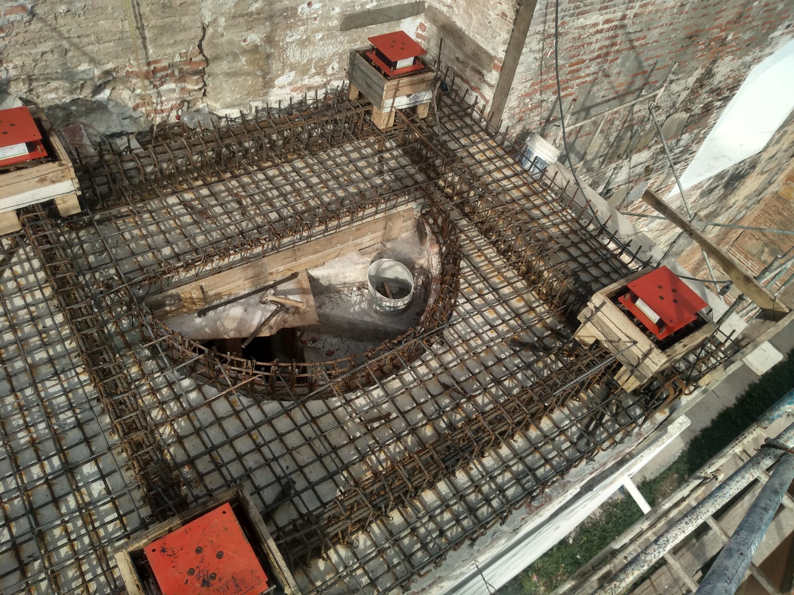 Instalación real de un aislador sísmico elastomérico con placa roja en la base de un campanario histórico de mampostería — proyecto VELATOPH®
